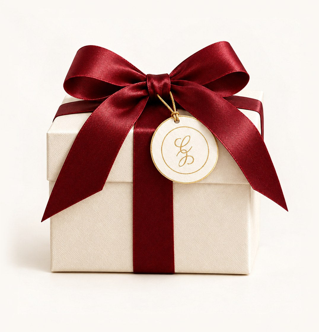 Geschenkbox in elfenbeinfarbenem Strukturpapier mit granatroter Seidenschleife und goldgeprägtem Christelle-Anhänger